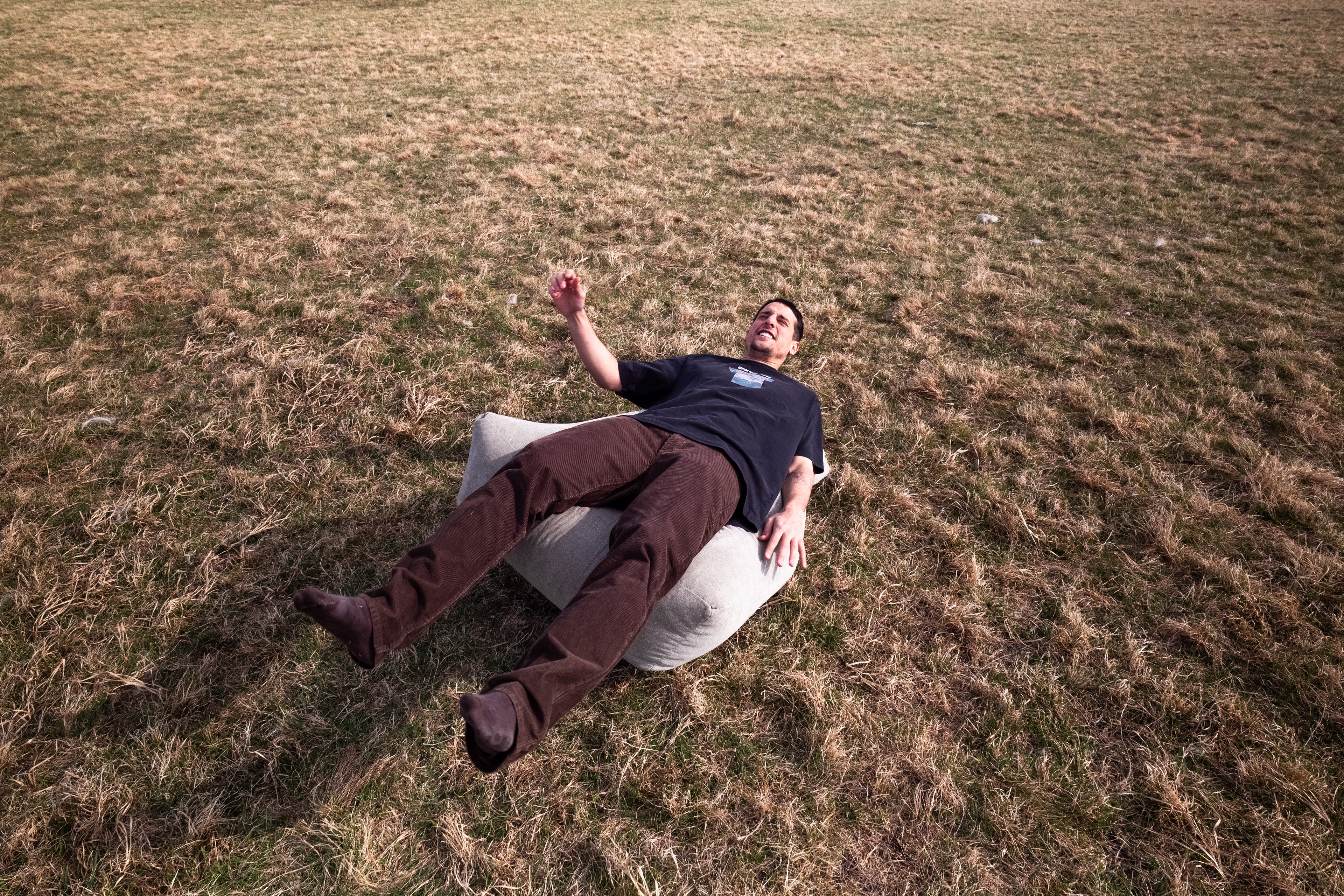 Person lying on a bean bag chair in a grassy field with vintage black tshirt