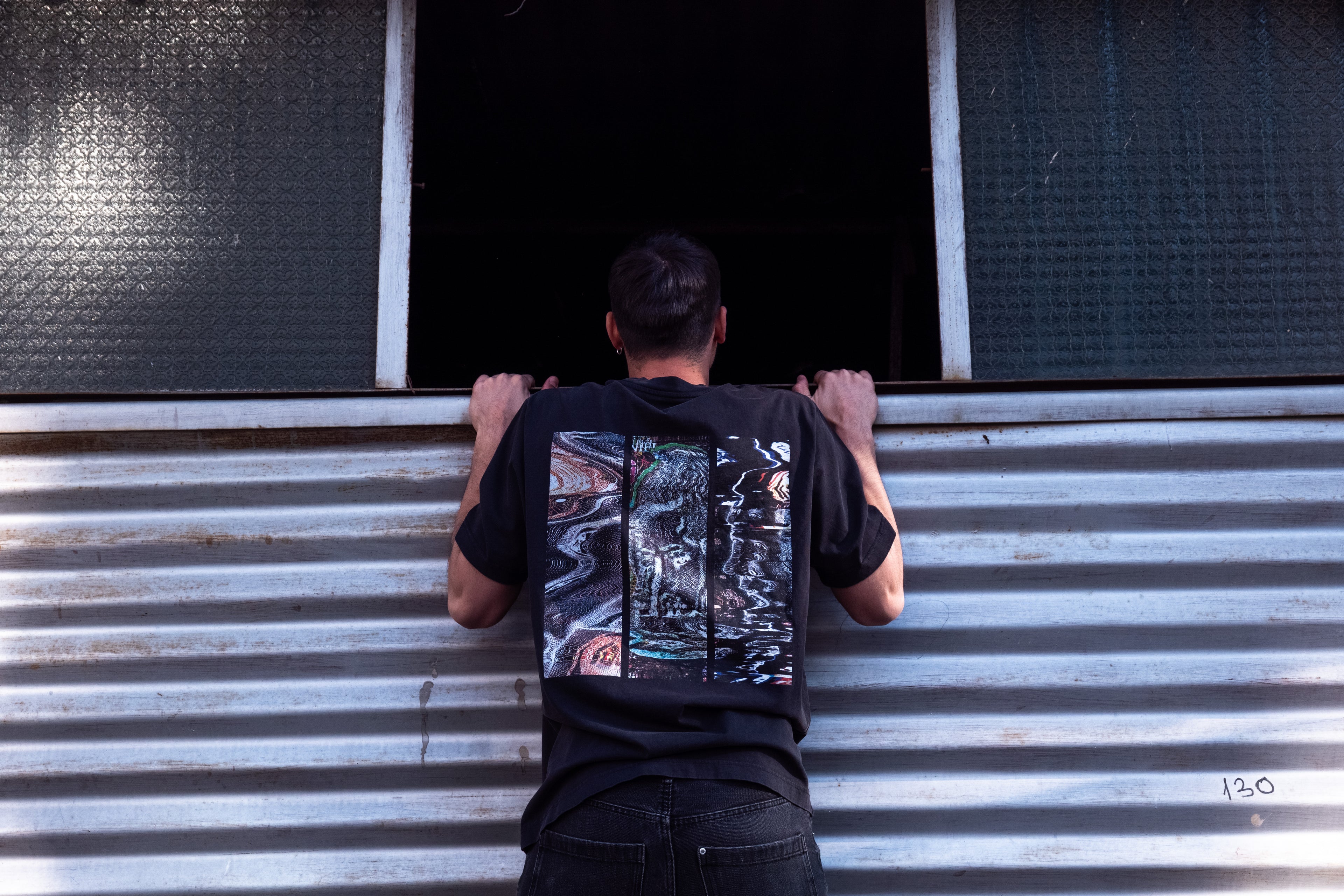 man with a DTG trippy printed t-shirt peeking inside a dark garage through a window
