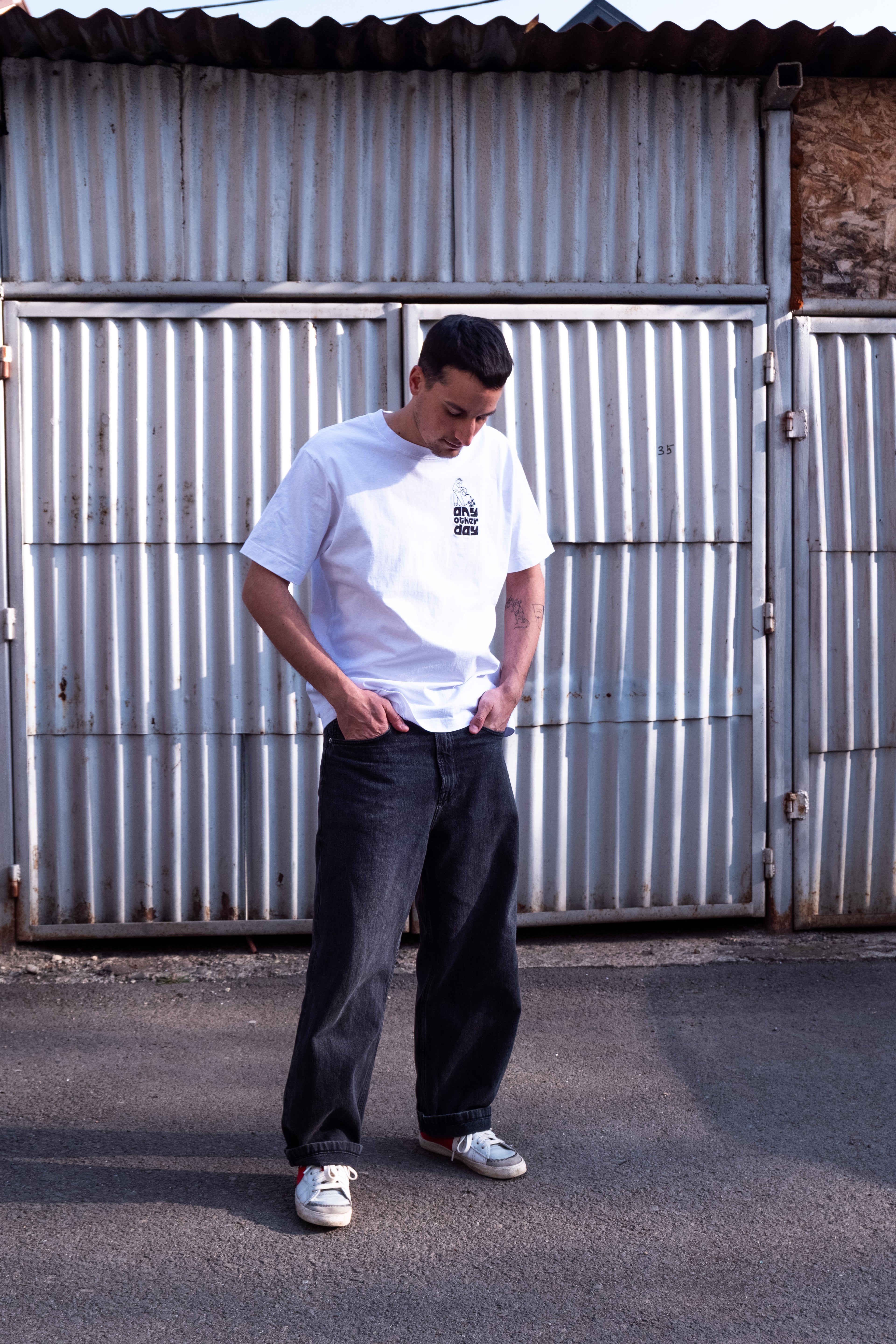 man posing with white cotton t-shirt and dark gray jeans in front of a garage door